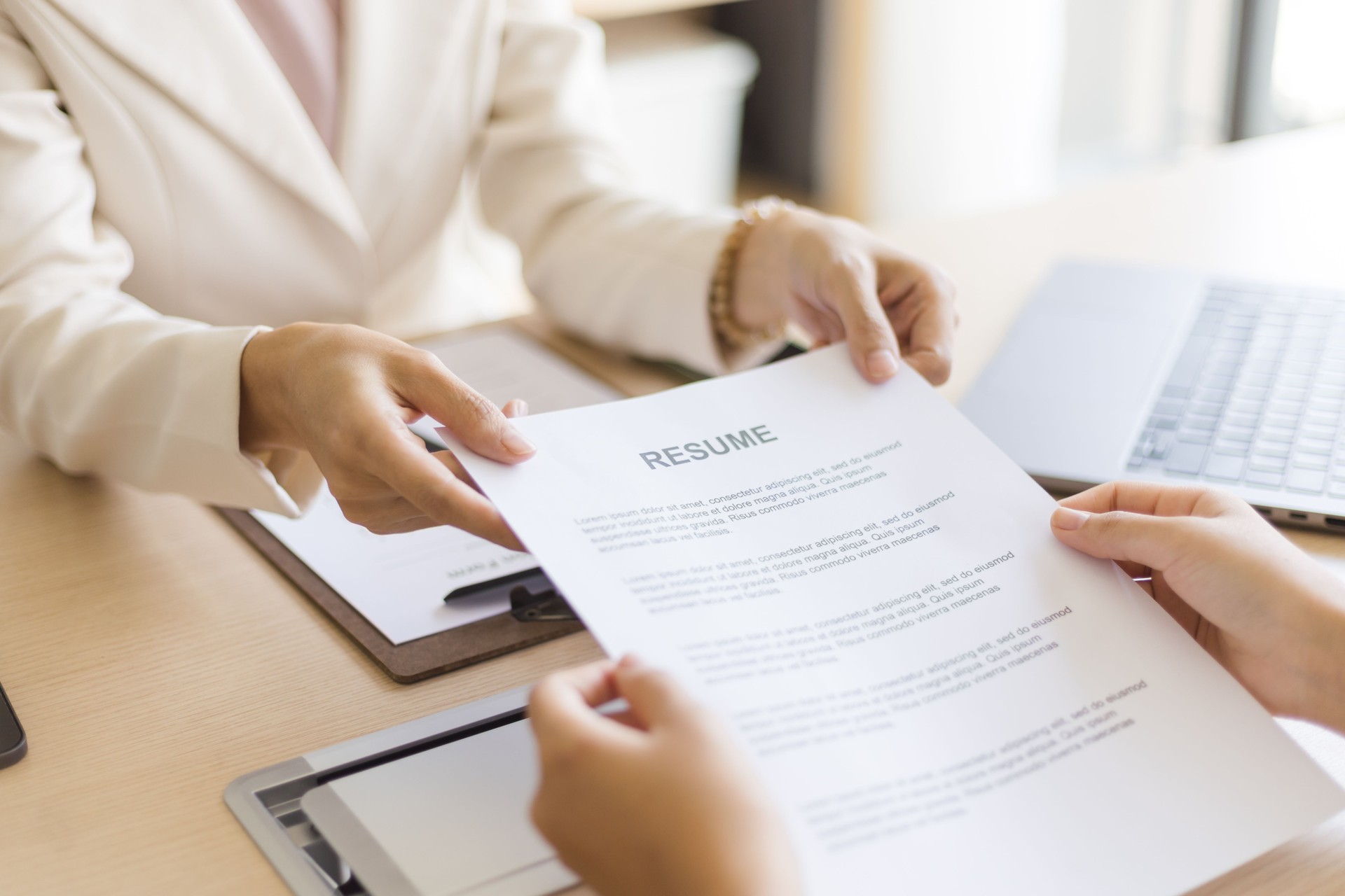 Close-up of two businesswomen holding resume documents in a meeting room.